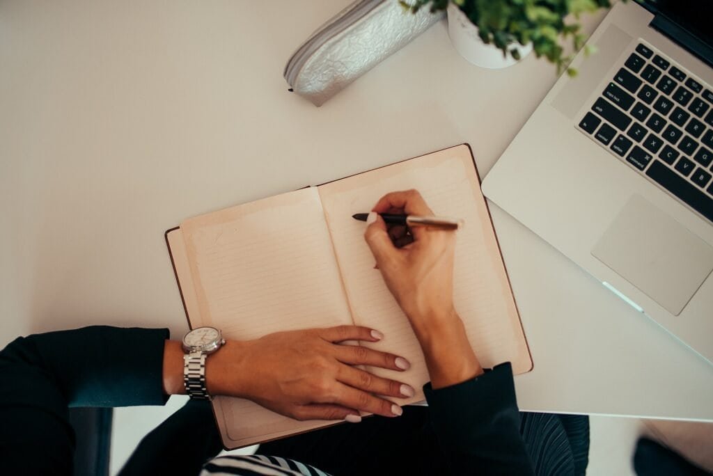 Person writing notes while reviewing content on a laptop, representing a content quality audit