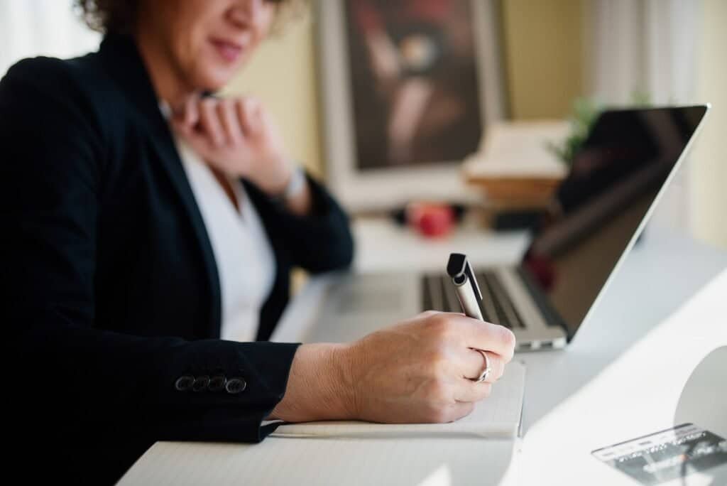 Business professional taking notes at a desk during a meeting, representing preparation for a performance review