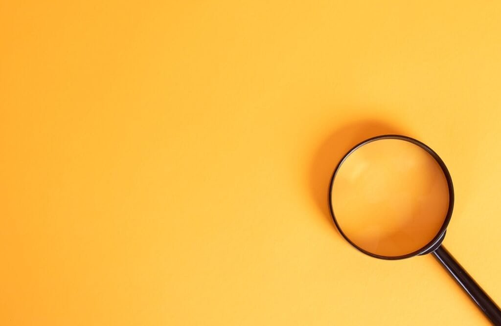 A magnifying glass on a yellow background representing search engine results and meta descriptions