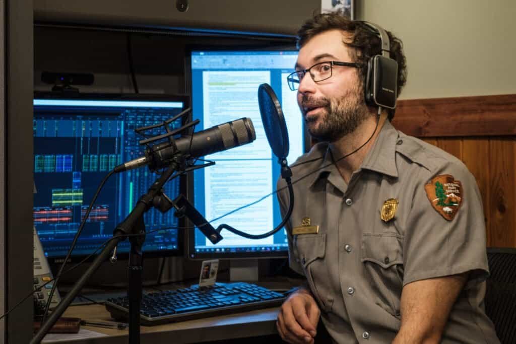 Person recording a podcast episode in front of a microphone and computer screens, representing repurposing content into multiple formats