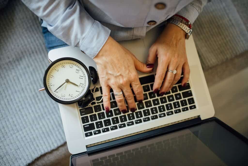 Hands typing on a laptop with a clock beside it, representing time spent triaging an email inbox