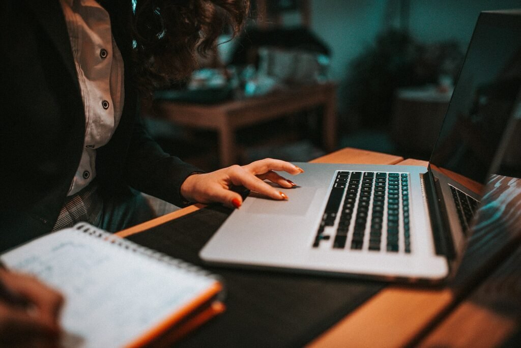 Person typing on a laptop keyboard while writing notes for research