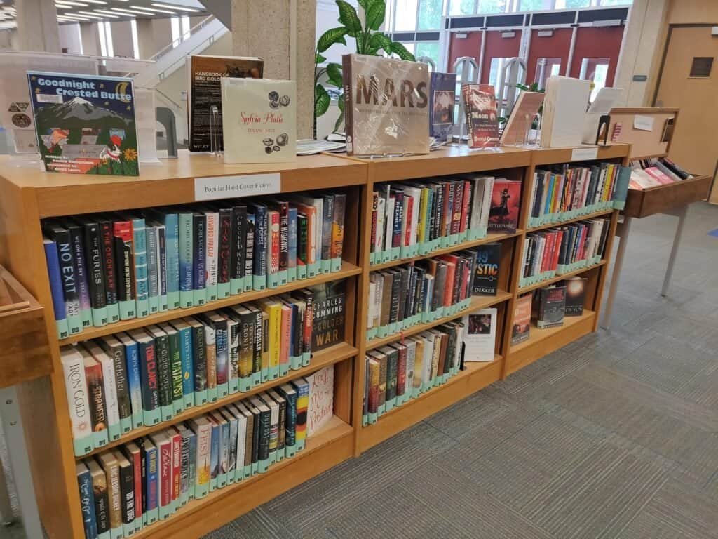Rows of books on a library shelf with color-coded labels
