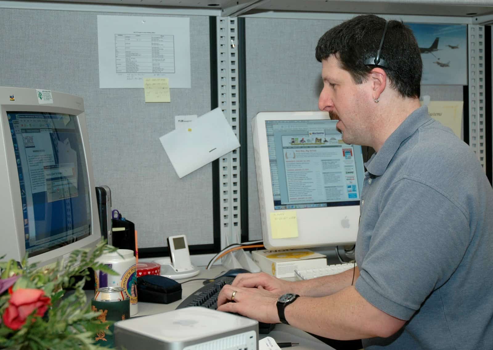 Man wearing a headset answering a phone call while typing at a keyboard