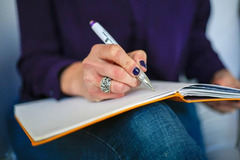 Person writing a weekly review and planning next steps in a notebook